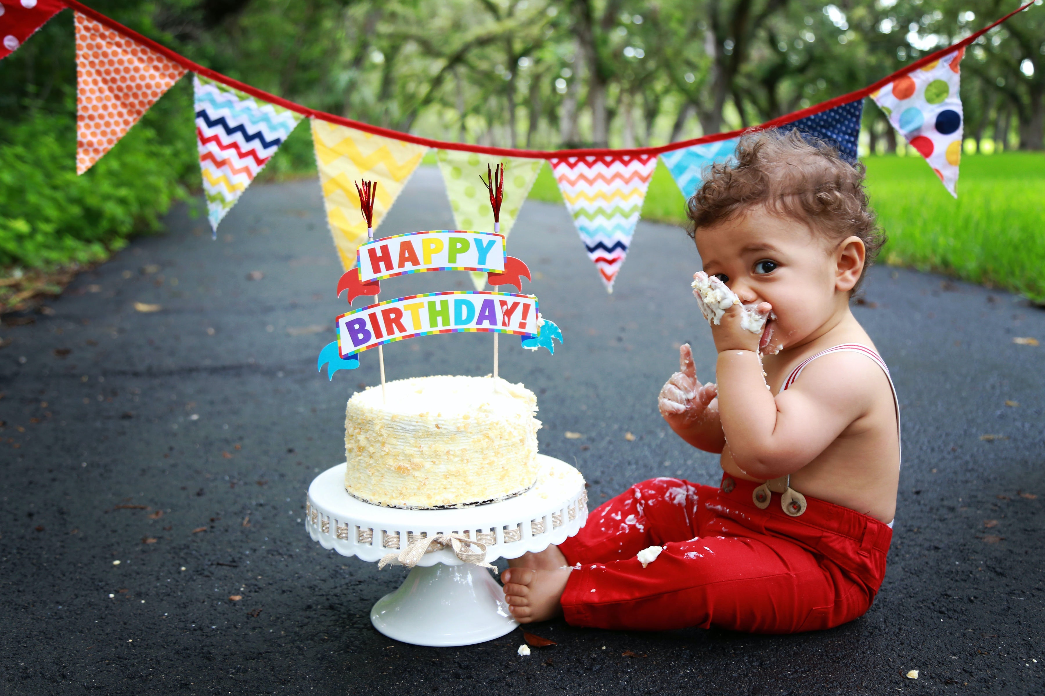Baby eating birthday cake with a happy birthday sign and bunting in the background