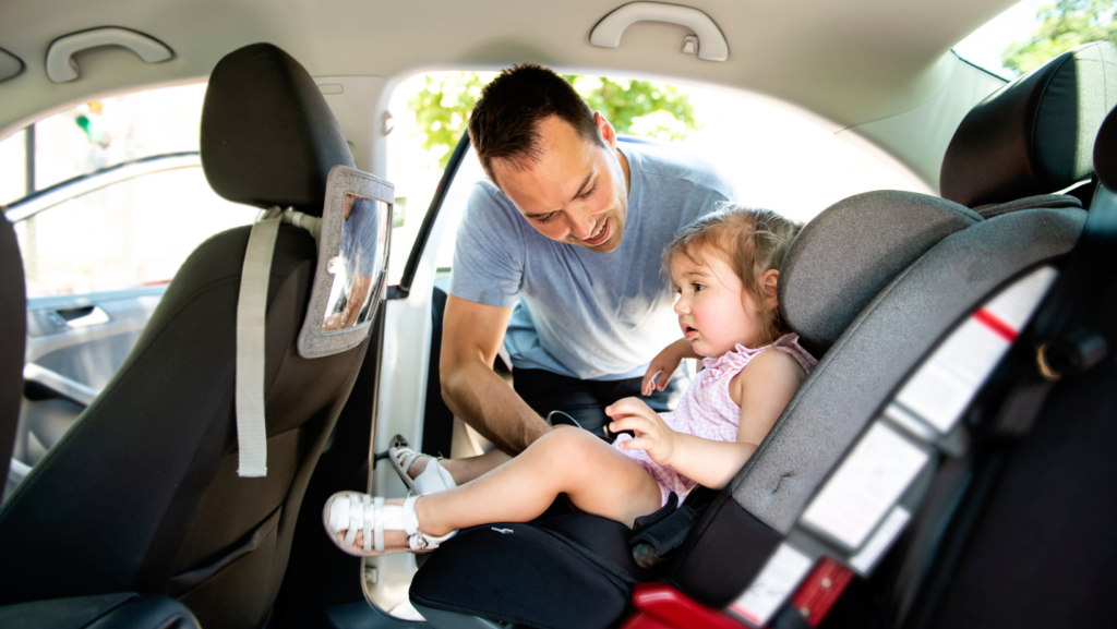 Man buckling a young girl into her car seat