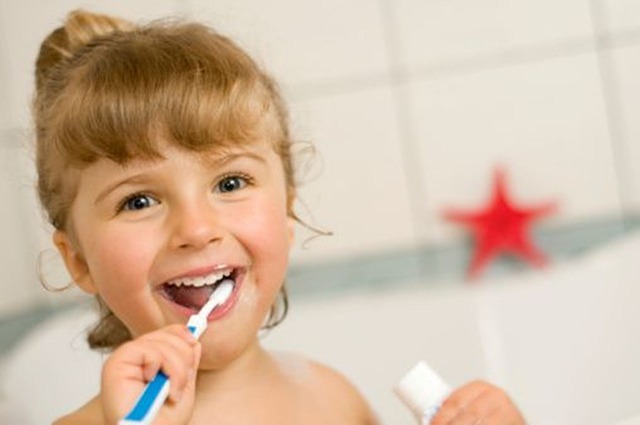 toddler brushing teeth smiling and holding toothpaste