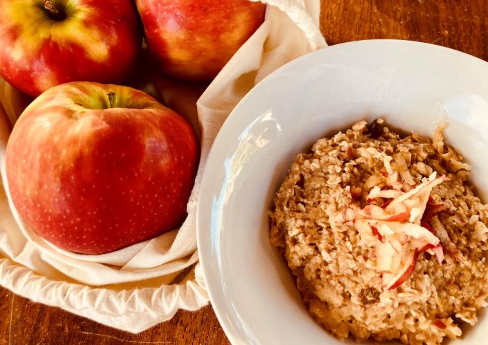 Bowl of apple and cinnamon porridge next to a bag of apples