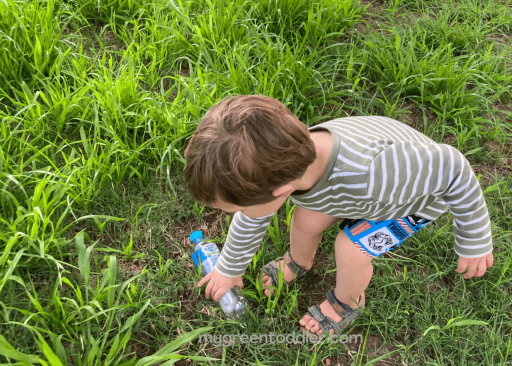 Boy picking up a plastic bottle from the grass