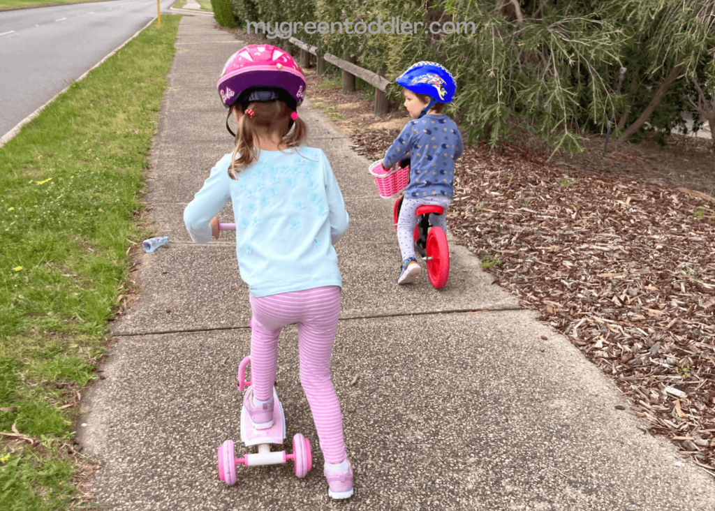 A girl riding a scooter and a boy riding a bike