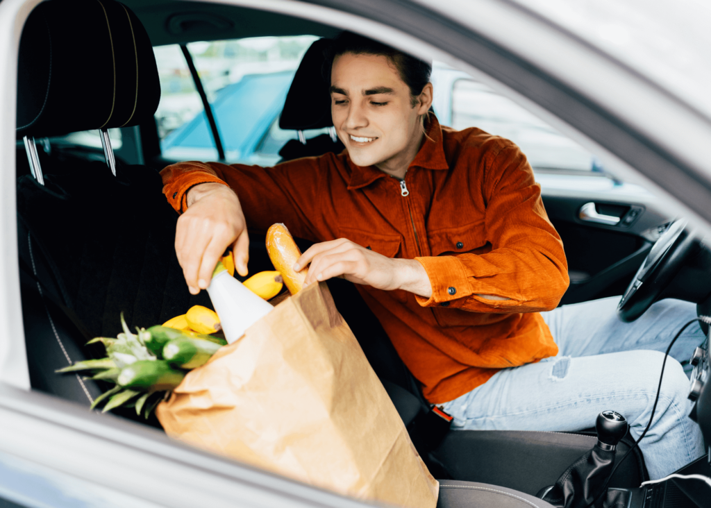 Man in car with paper bag full of groceries in passenger seat